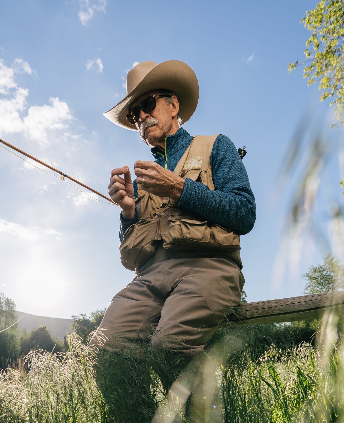 Man tying a fishing fly outdoors wearing CliC sunglasses